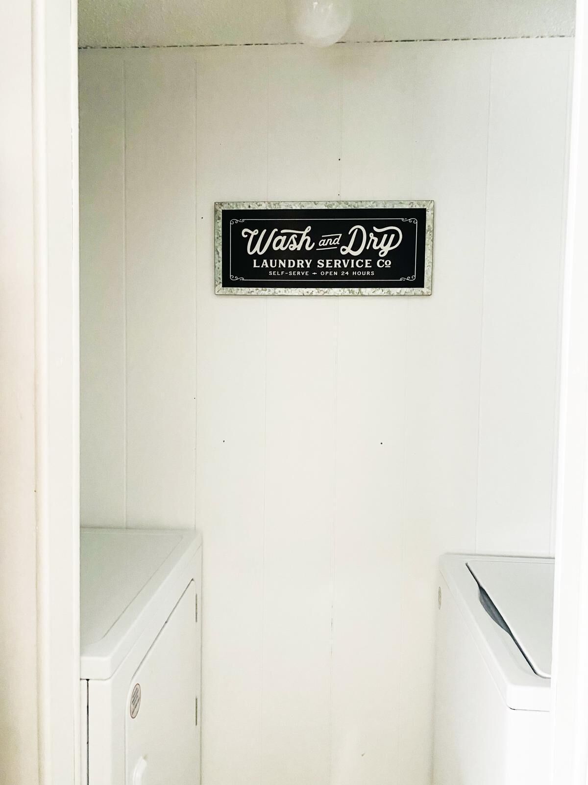 Een wasserette met een bordje waarop staat: 'Wash and Dry Laundry Service Co. Zelfbediening, 24 uur per dag geopend'.