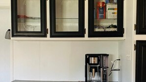 Una cocina con armarios negros, una cafetera y una estantería con objetos.