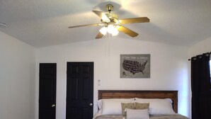 Un dormitorio con una cama, un ventilador de techo, una puerta negra y un mapa mural.
