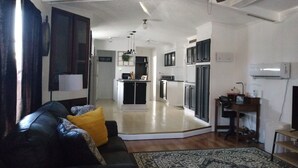 Una sala de estar con un sofá de cuero negro, un tapete estampado y un ventilador de techo.