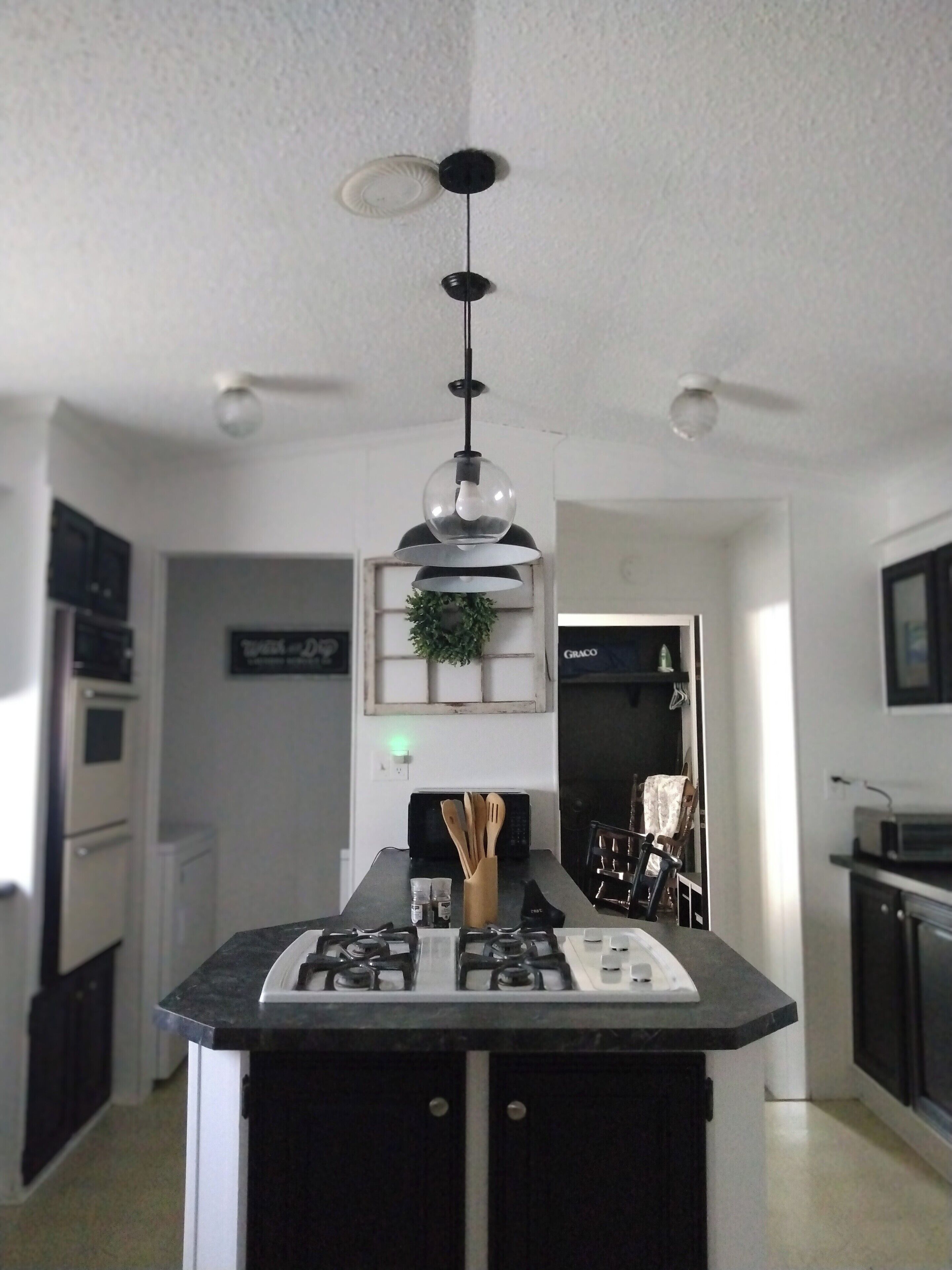 A modern kitchen with a central island, black cabinets, stainless steel appliances, and a pendant light.