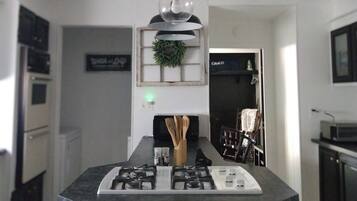 A modern kitchen with a central island, black cabinets, stainless steel appliances, and a pendant light.