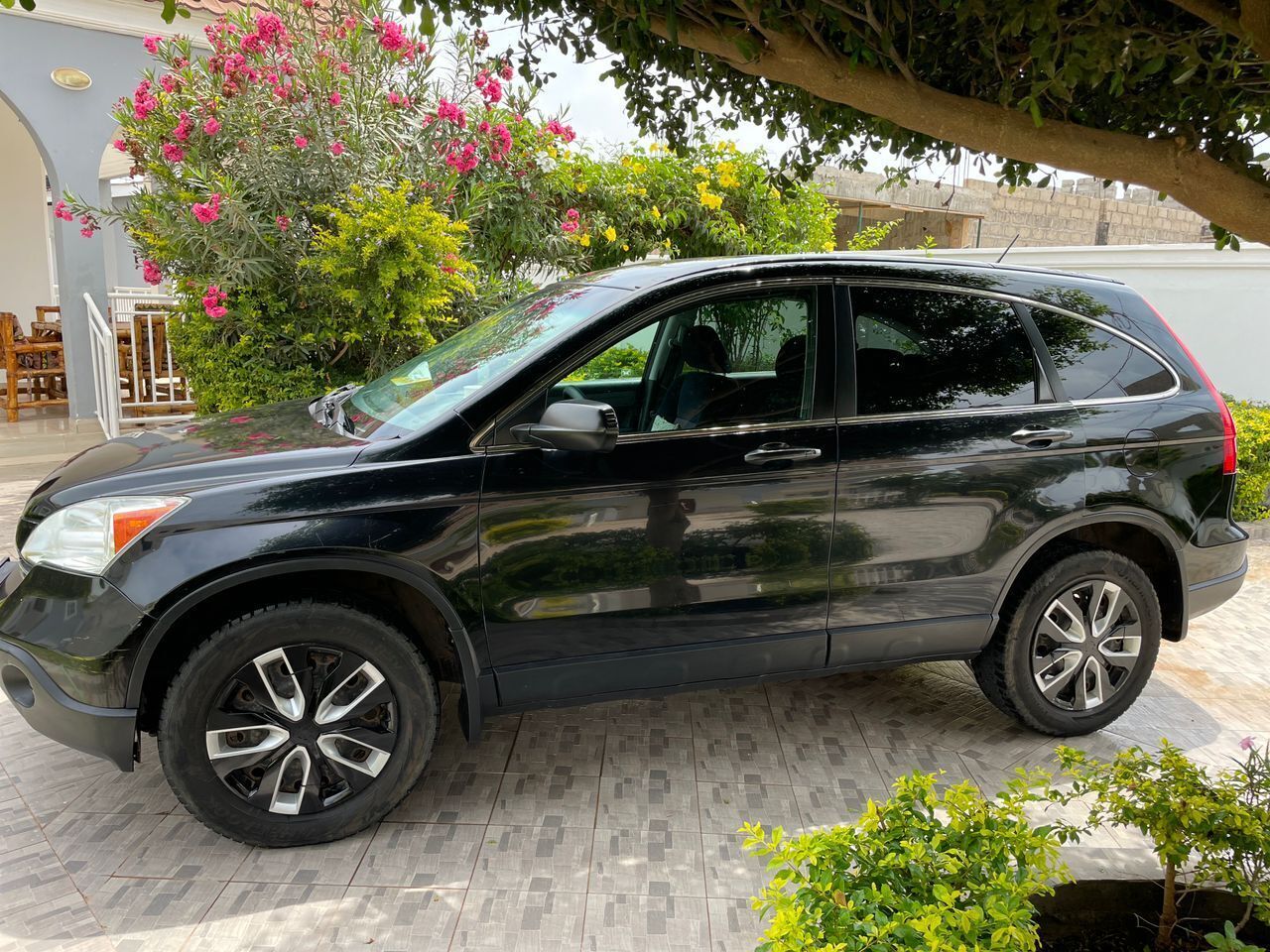 Ein schwarzer SUV parkt auf einem befestigten Platz, im Hintergrund befinden sich ein Garten und ein Gebäude.