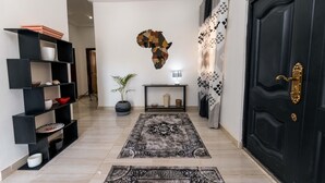 Un pasillo con una puerta negra, una consola negra, una planta en maceta y una alfombra estampada.