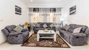 Una sala de estar con dos sofás grises, una mesa de centro, alfombra estampada y una guitarra.