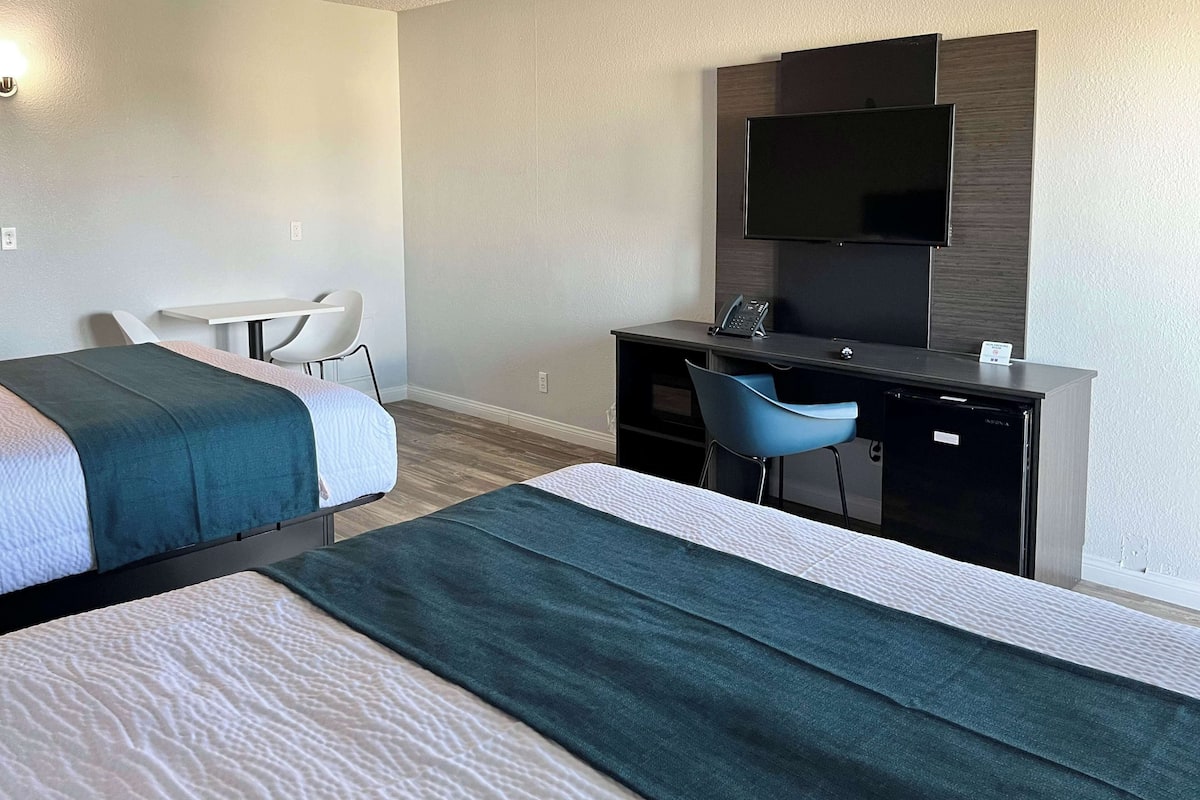 A hotel room with two beds, a desk, a chair, a TV, and a minibar.