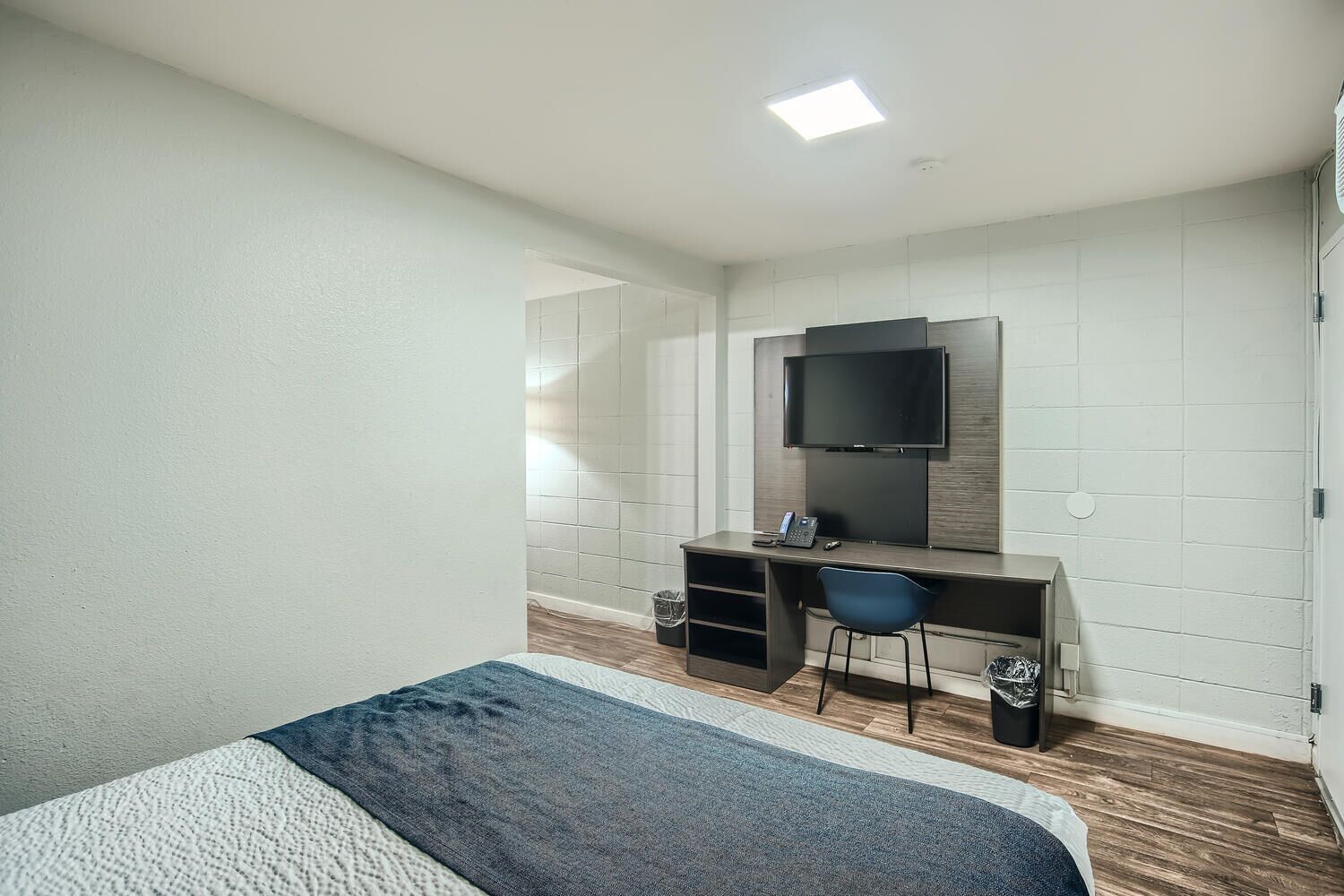 A hotel room with a bed, a desk, a chair, a television, and a trash bin.