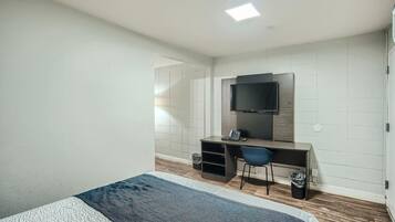A hotel room with a bed, a desk, a chair, a television, and a trash bin.