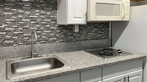 Una cocina con encimera de granito, pileta de acero inoxidable, gabinetes blancos, microondas y estufa.