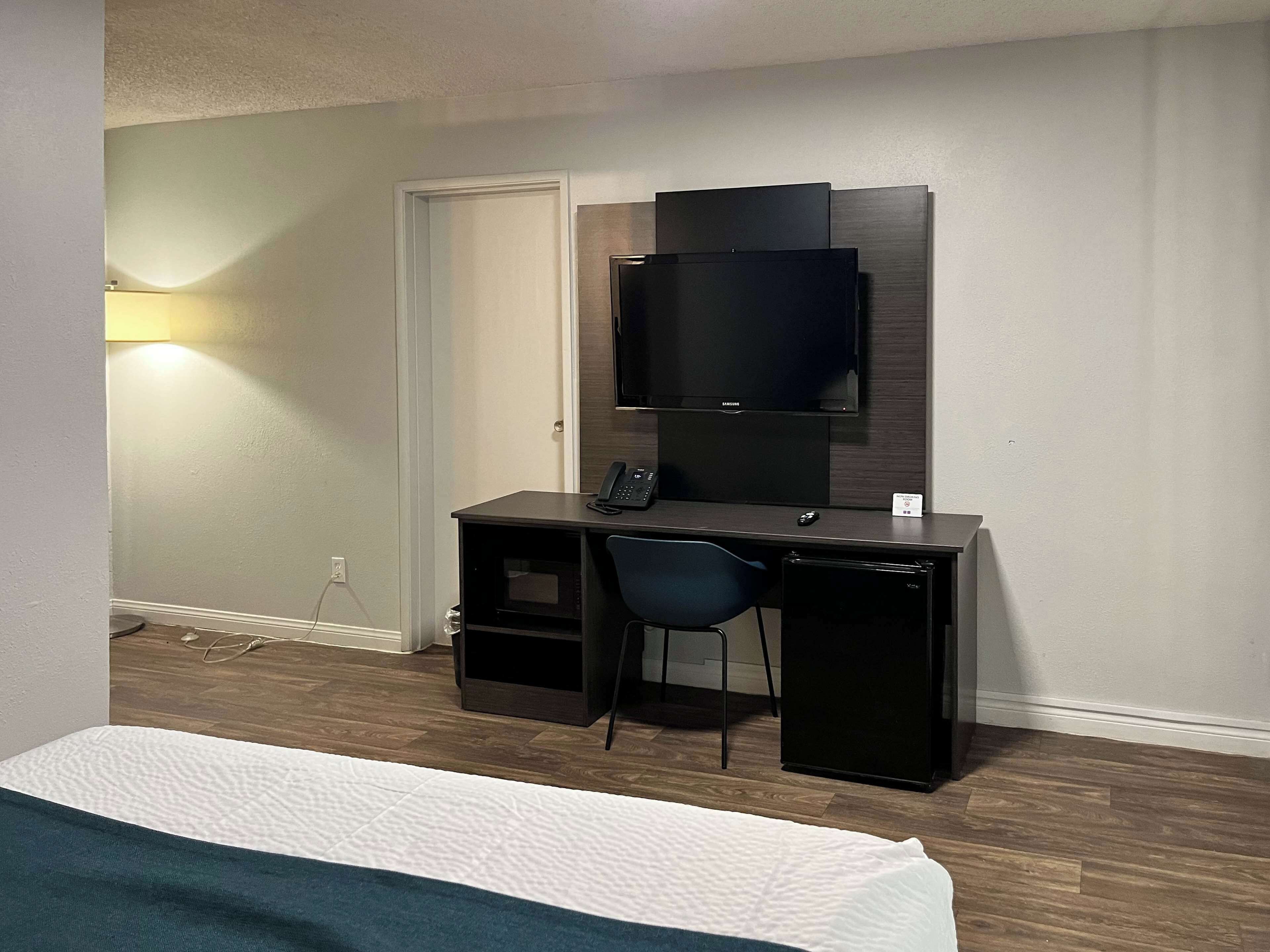 Ett hotellrum med en säng, ett skrivbord med en stol, en platt-TV och en lampa.