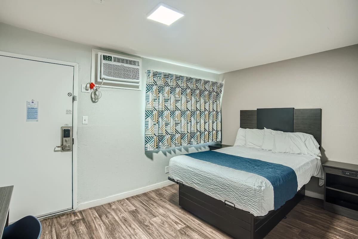 A hotel room with a bed, a nightstand, a desk, a chair, a wardrobe, and a patterned curtain.