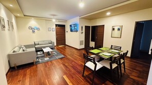Amplia sala de estar con comedor, piso de madera, un sofá gris y una mesa de comedor para cuatro comensales.