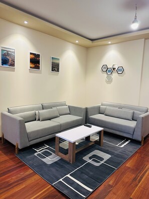 A modern living room with a grey sectional sofa, a small white table, and a geometric patterned rug.