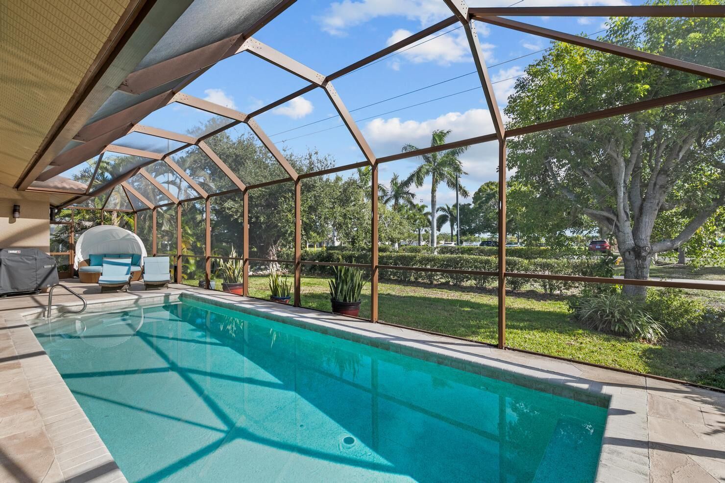 A swimming pool with a glass enclosure, lounge chairs, and a view of a landscaped garden.