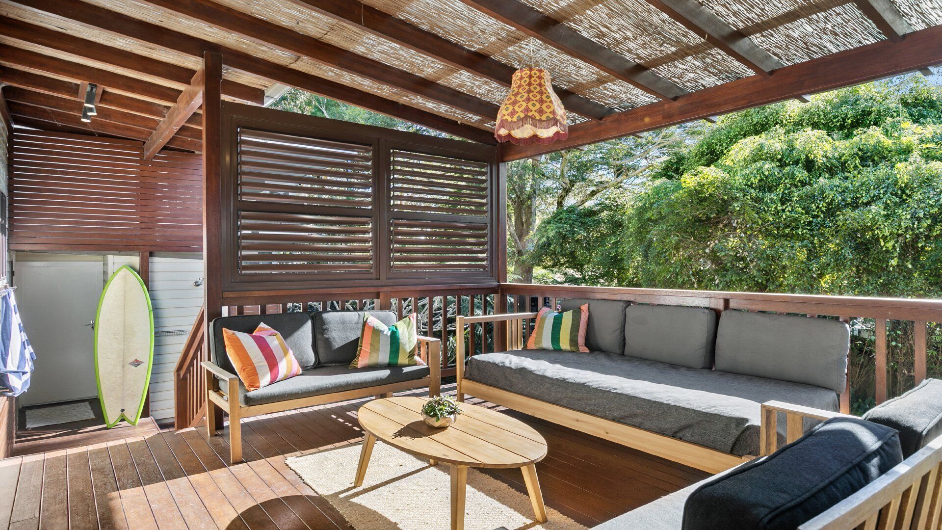 An outdoor seating area with a wooden bench and a table, surrounded by a wooden pergola with a woven ceiling.