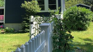 A dark blue house with a white picket fence, a small porch, and a window with shutters. - Down the road from Bayview Beach on Ferry Rd! Bright, and newly furnished 2 BR. (Saco)