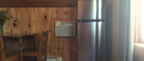 A compact kitchen with wooden walls, a stainless steel refrigerator, a wooden dining table with chairs, and a patterned rug.