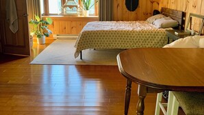 A cozy wooden cabin bedroom with a large bed, a dining table, and a window with curtains. - Down the road from Bayview Beach on Ferry Rd! Bright, and newly furnished 2 BR. (Saco)