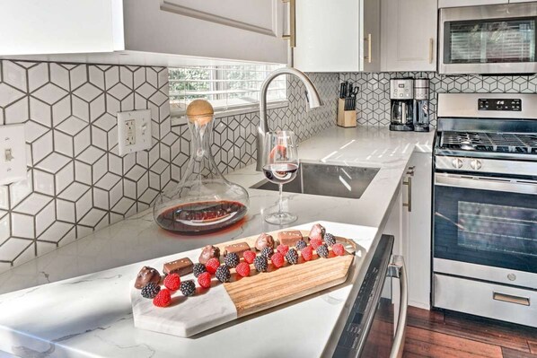 A kitchen with a marble countertop, a wine glass, and a tray of assorted chocolates and berries.