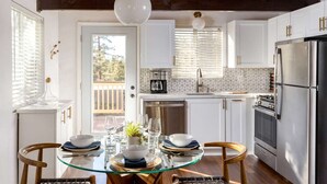 A modern kitchen with white cabinets, a stainless steel refrigerator, and a glass dining table set for two.