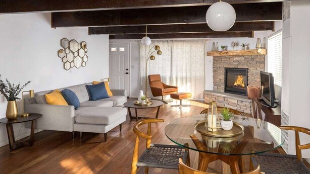 A modern living room with a sofa, armchairs, a glass coffee table, a fireplace, and a television.