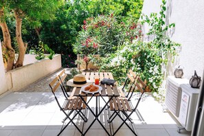 A patio with a wooden table and chairs, a hat, a book, and a plate of food. - Procy-106 Venus Townhouse (Paphos)