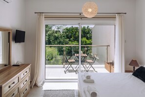 A bedroom with a large bed, a TV mounted on the wall, a wooden dresser, and a balcony with chairs and a table. - Procy-106 Venus Townhouse (Paphos)