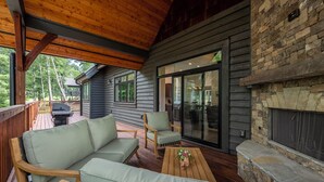Une terrasse couverte avec un plafond en bois, une cheminée en pierre et un coin salon comprenant un canapé et des fauteuils.