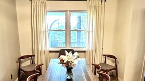 En spisestue med et træbord, seks stole, en vase med blomster og et vindue med gardiner.