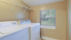 A laundry room with a washer and dryer, a metal drying rack, and a window with blinds. - Delightful 2-bedroom, 1-bath Home Near Biloxi's Scenic Back Bay (Biloxi)