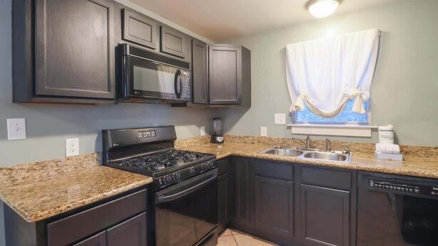 A kitchen with dark cabinets, a granite countertop, a stove, a microwave, and a dishwasher. - Delightful 2-bedroom, 1-bath Home Near Biloxi's Scenic Back Bay (Biloxi)