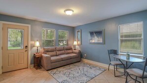 A living room with a beige sofa, two side tables with lamps, a patterned rug, a dining table with chairs, and a window with blinds. - Delightful 2-bedroom, 1-bath Home Near Biloxi's Scenic Back Bay (Biloxi)