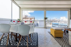 A balcony with a dining table set for four, a yellow ottoman, and a view of the cityscape.