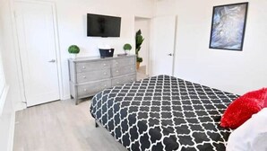 Et soveværelse med seng, kommode, loftventilator, fjernsyn og en dør.
