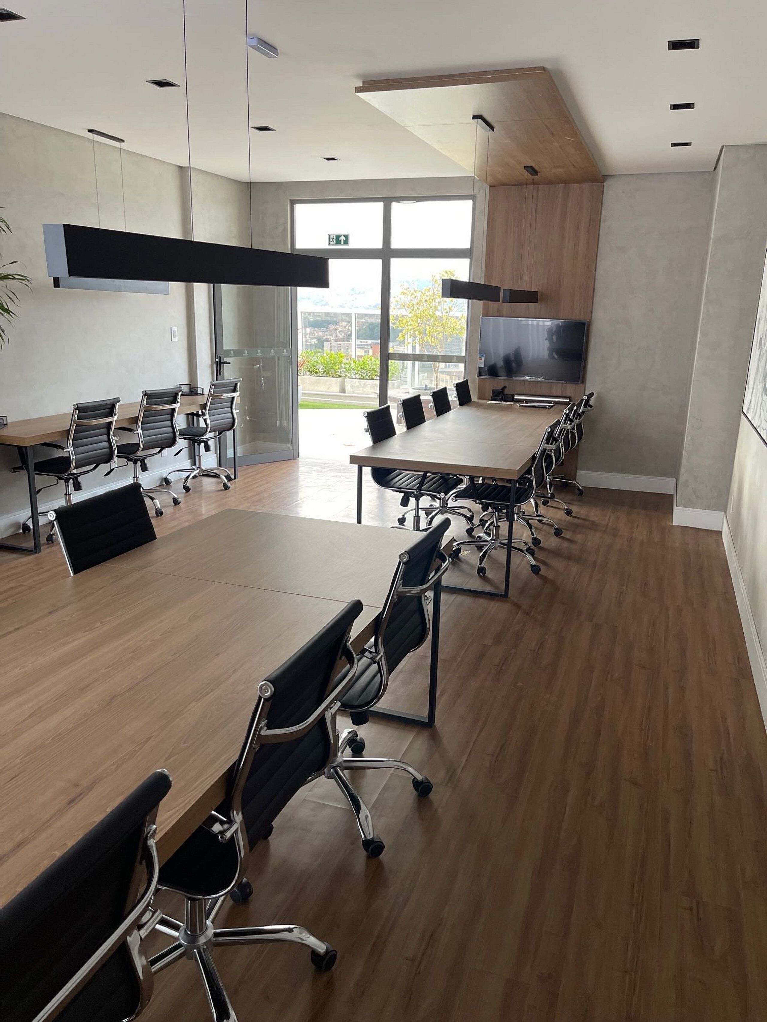 A modern conference room with a large table and black office chairs, large windows, and a flat-screen TV.