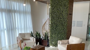 Uma sala de estar moderna com um conjunto de sofá, uma mesa de centro e uma cadeira suspensa. Há uma parede verde com plantas e teto de madeira.