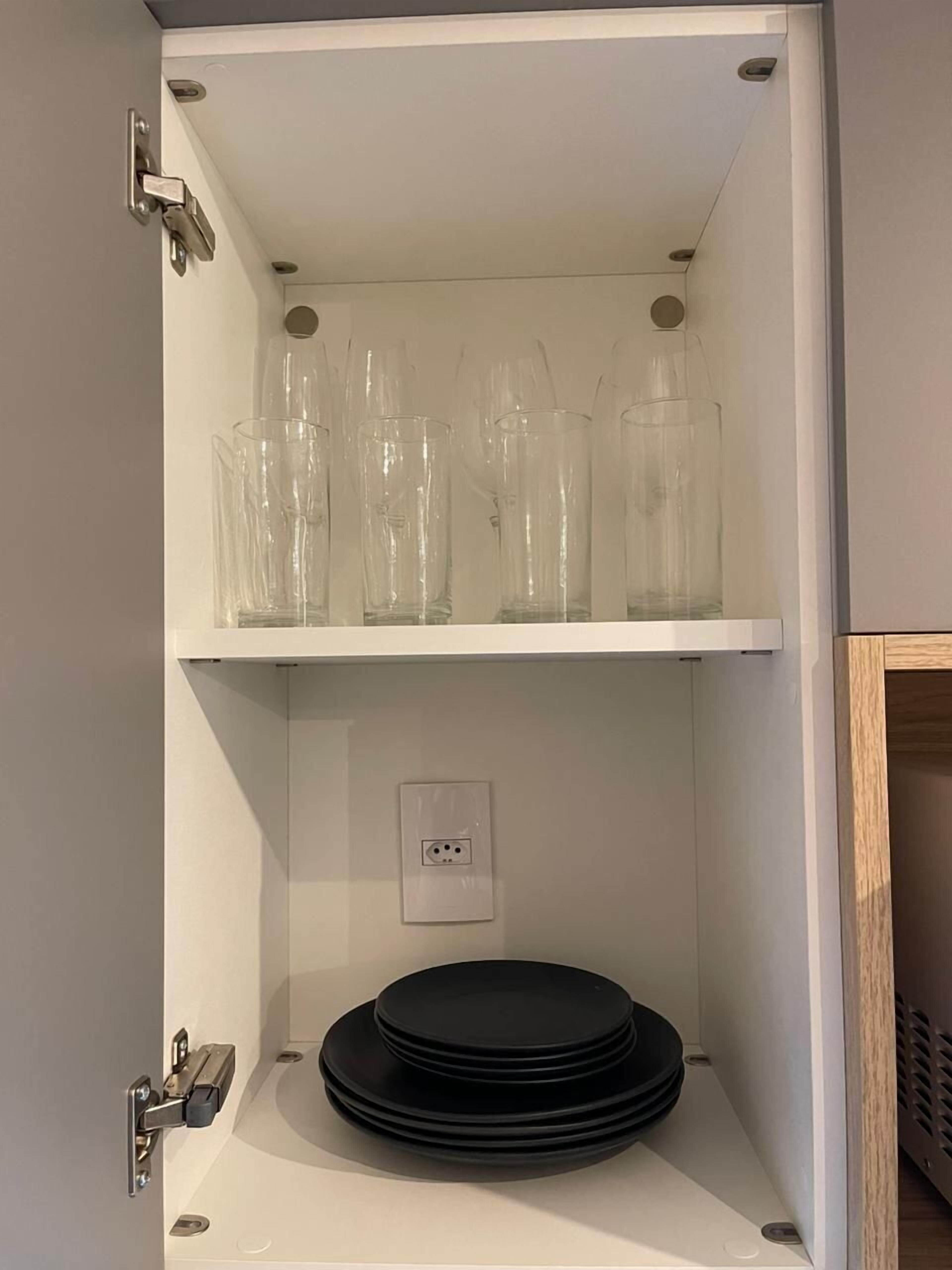 A storage unit with shelves containing clear plastic cups and black plates.