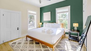 A bedroom with a bed, a ceiling fan, a window, a nightstand, and a mirror. - Aerie Loft: Cozy 1-bedroom Retreat in Biloxi, Perfect for Couples! (Biloxi)