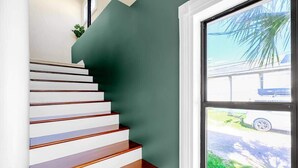 A staircase with white steps and dark wood handrails, leading to a room with a green wall and a window overlooking a street. - Aerie Loft: Cozy 1-bedroom Retreat in Biloxi, Perfect for Couples! (Biloxi)