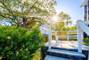 A wooden deck with a white railing, surrounded by lush greenery and a large tree. - Retreat at Aerie Loft (Biloxi)
