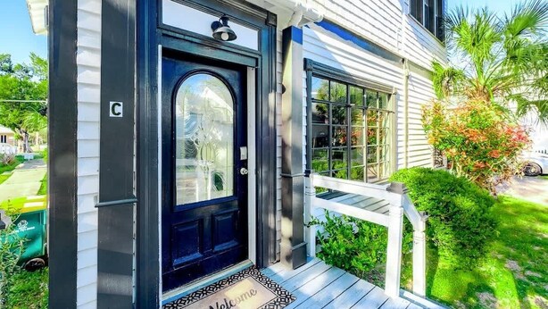 A house with a black front door, a white porch, and a small garden with a palm tree. - Aerie Loft: Cozy 1-bedroom Retreat in Biloxi, Perfect for Couples! (Biloxi)