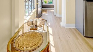 A kitchen with a stainless steel refrigerator, a dining area with a glass table and wicker chairs, and a view through a large window. - Aerie Loft: Cozy 1-bedroom Retreat in Biloxi, Perfect for Couples! (Biloxi)