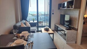 A modern hotel room with a dining area, a sofa, a TV, and a balcony with a city view. - B402- 1 Bedroom Condo With Sea View, Ao Nang Beach (Krabi)