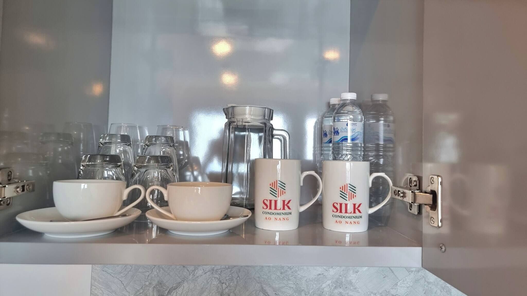 Una encimera de cocina con una cafetera, dos tazas, una taza grande y botellas de agua.