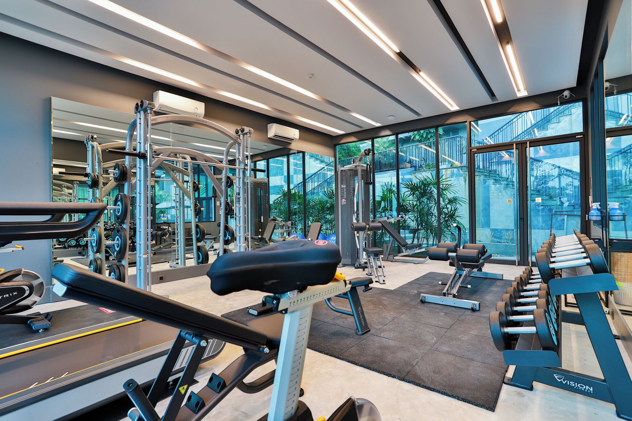 A modern gym with various exercise equipment, large windows, and a view of a bridge.