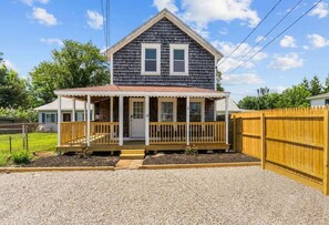 A two-story house with a porch, a fenced yard, and a gravel driveway.