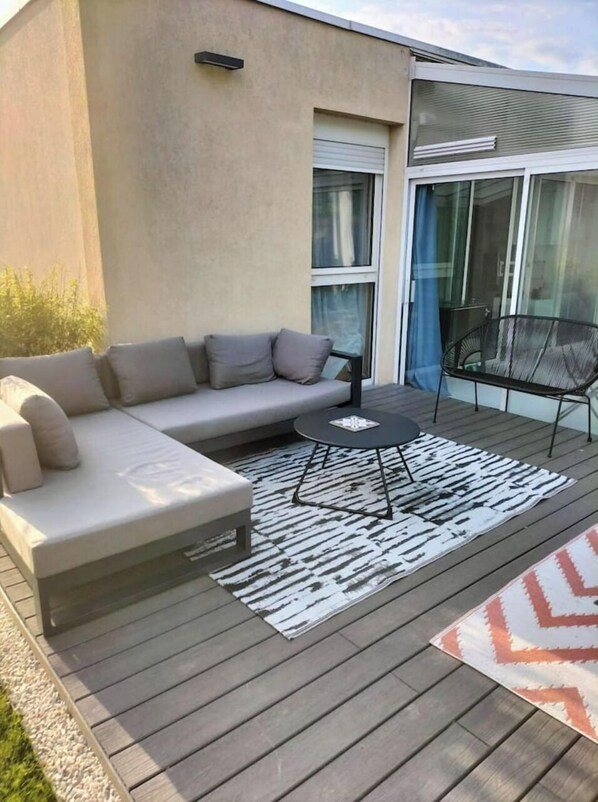 A modern outdoor living space with a grey sectional sofa, a round coffee table, and a patterned rug on a wooden deck.