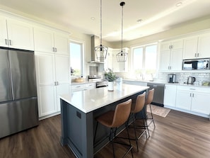 A modern kitchen with white cabinetry, stainless steel appliances, and a central island with bar stools. - 4 Bedroom Luxury Ocean View Beach House, Minutes To North Shore Beaches (Park Corner)