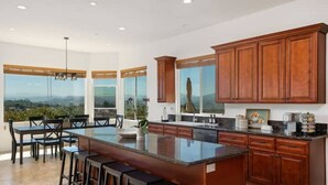 Una cocina amplia con una isla grande, armarios de madera y ventanas grandes que ofrecen vistas al exterior.