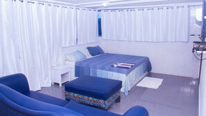 A bedroom with a bed, a blue sofa, a small table, and a colorful ottoman. - Hôtel Amazone (Cotonou)